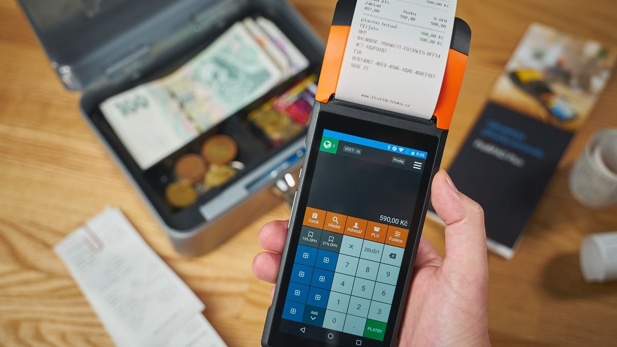 Perangkat pembayaran genggam mencetak struk dengan uang tunai dan koin di sekitarnya